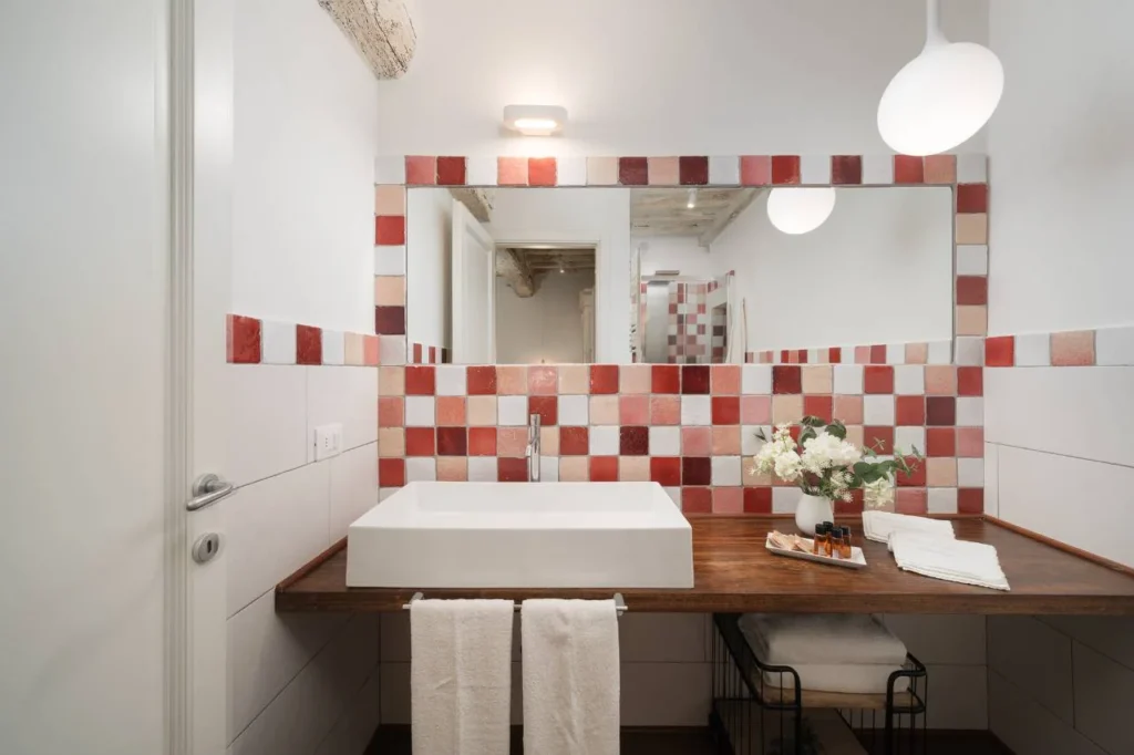 Bagno del B&B con lavabo moderno, grande specchio e parete decorata con piastrelle rosse e bianche