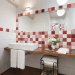 Bagno del B&B con lavabo moderno, grande specchio e parete decorata con piastrelle rosse e bianche